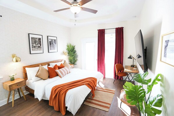 A bedroom with a bed, bedside tables, a desk, a chair, a television, and a plant.