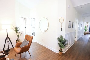 A modern living room with a wooden floor, a leather armchair, a standing lamp, and several potted plants. - The Champion's Suite. New Build, Upscale, Central (Gainesville)