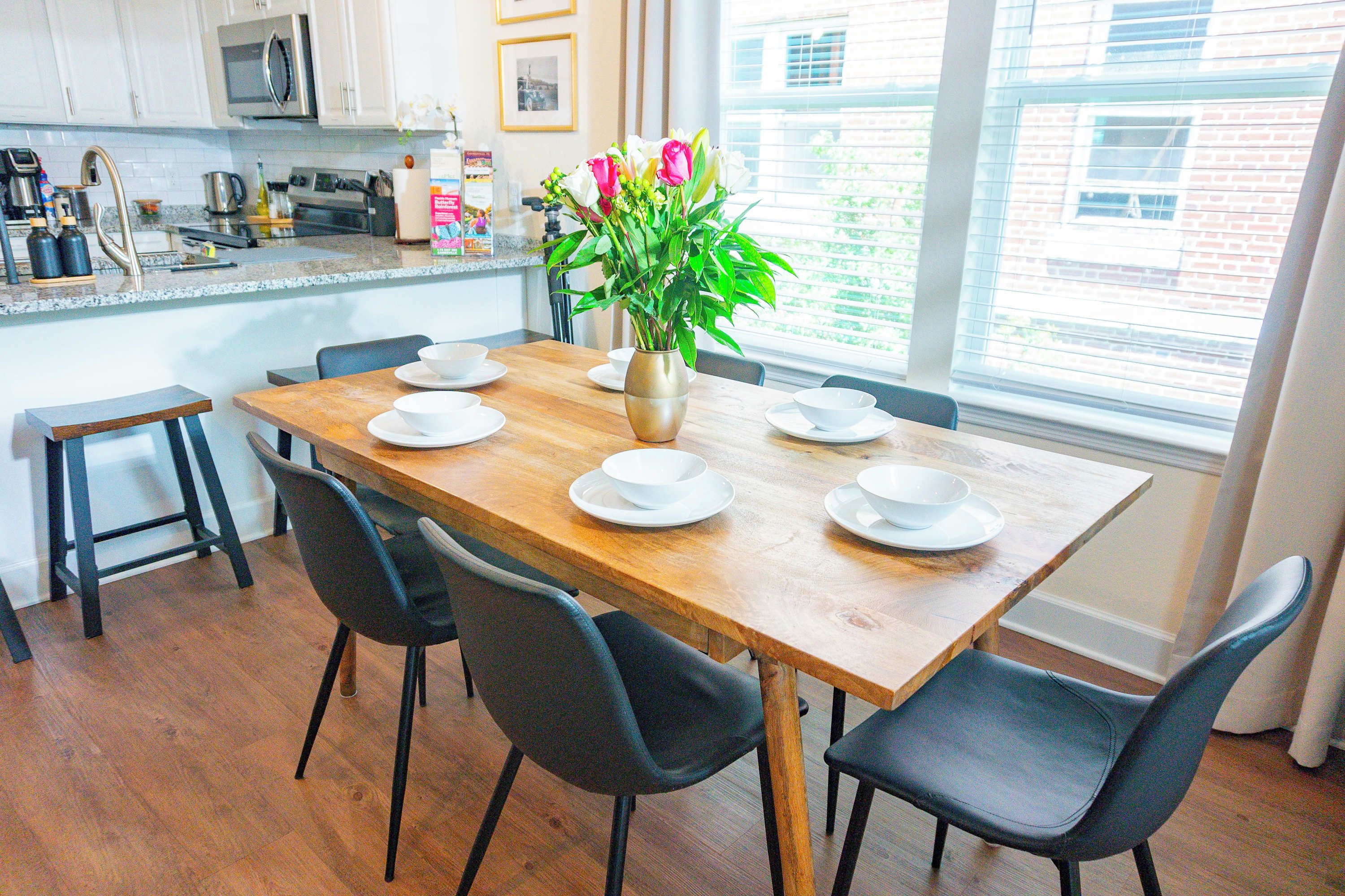 A dining area with a wooden table set for four, surrounded by black chairs, and a vase with flowers on the table.