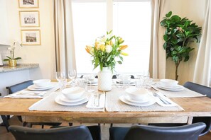 A dining table set with white plates, glasses, and cutlery, surrounded by black chairs.
