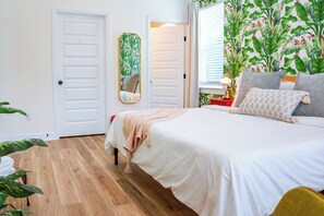 Un dormitorio con cama, espejo, ventana con cortinas, planta y puerta.