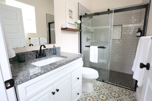 A bathroom with a granite countertop, white sink, and a glass shower enclosure. - The Royal Crane Suite, New Build, Upscale, Central (Gainesville)