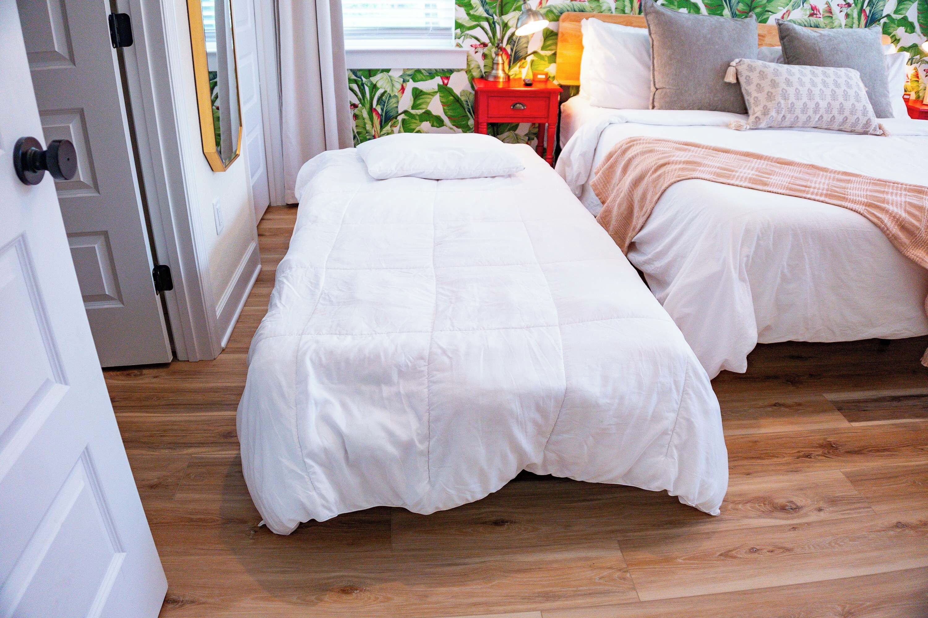 Une chambre avec deux lits, une table de chevet rouge et une fenêtre donnant sur un paysage verdoyant.
