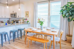 A modern kitchen with white cabinets, stainless steel appliances, and a wooden dining table set with white plates and cups. - The Royal Crane Suite, New Build, Upscale, Central (Gainesville)