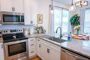 A modern kitchen with white cabinets, stainless steel appliances, granite countertops, and a dining area with a table and chairs. - The Royal Crane Suite, New Build, Upscale, Central (Gainesville)
