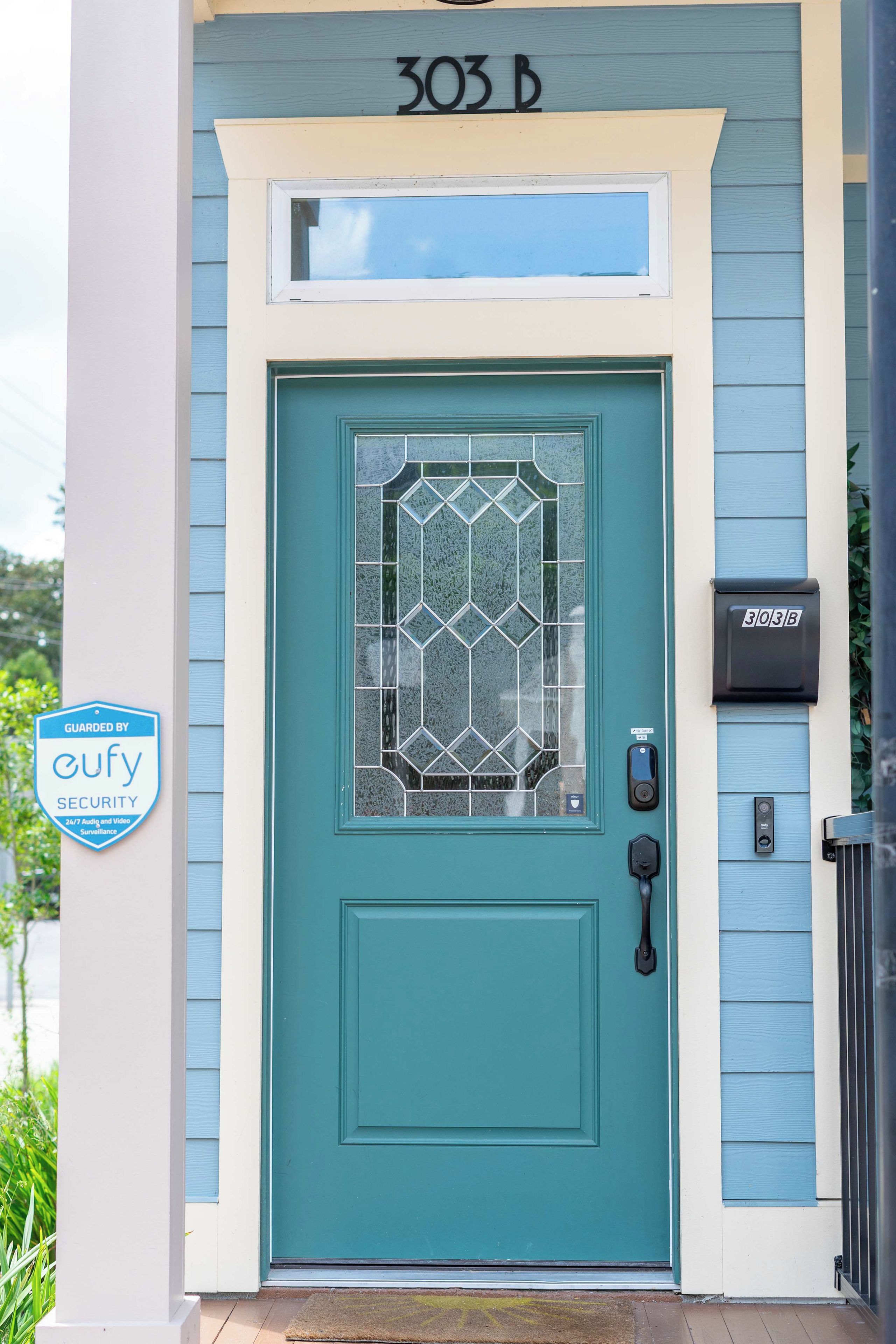 A teal door with a glass panel, a mailbox, and a 'GUARDED BY eufy SECURITY' sign.