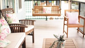 Een houten veranda met twee houten stoelen en een bank, elk met een kussen.