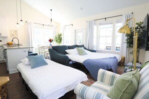 A modern hotel room with two beds, a dining area, and a kitchenette.