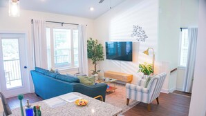 Een moderne woonkamer met een blauwe bank, een gestreepte fauteuil, een flatscreen televisie, een eethoek met een granieten aanrechtblad en een potplant.