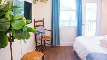 Un dormitorio con cama, una silla, una planta colgante y una ventana con cortinas.