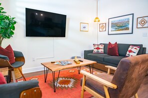 A modern living room with a flat-screen TV, a wooden coffee table, a sofa with patterned cushions, and a red rug. - The Prairie Suite. Newly Built, Upscale, Central (Gainesville)