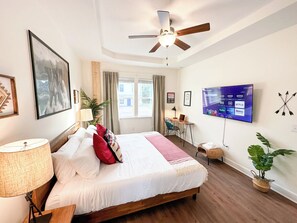A hotel room with a bed, a desk, a chair, a TV, and a ceiling fan.