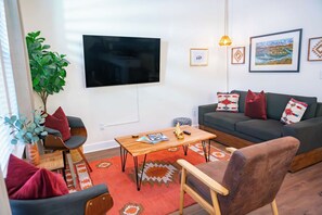 A living room with a flat-screen TV, a sofa, a coffee table, and a chair. - The Prairie Suite. Newly Built, Upscale, Central (Gainesville)