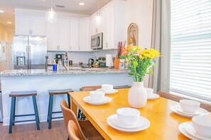 A modern kitchen with white cabinets, stainless steel appliances, and a wooden dining table set for four. - The Prairie Suite. Newly Built, Upscale, Central (Gainesville)