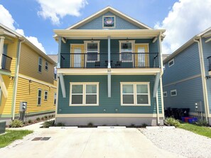 A two-story townhouse with a balcony on the second floor, a front porch, and a small garden area. - The Prairie Suite. Newly Built, Upscale, Central (Gainesville)