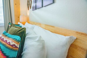 A neatly made bed with white and colorful pillows, a wooden headboard, and a wall-mounted lamp. - The Prairie Suite. Newly Built, Upscale, Central (Gainesville)
