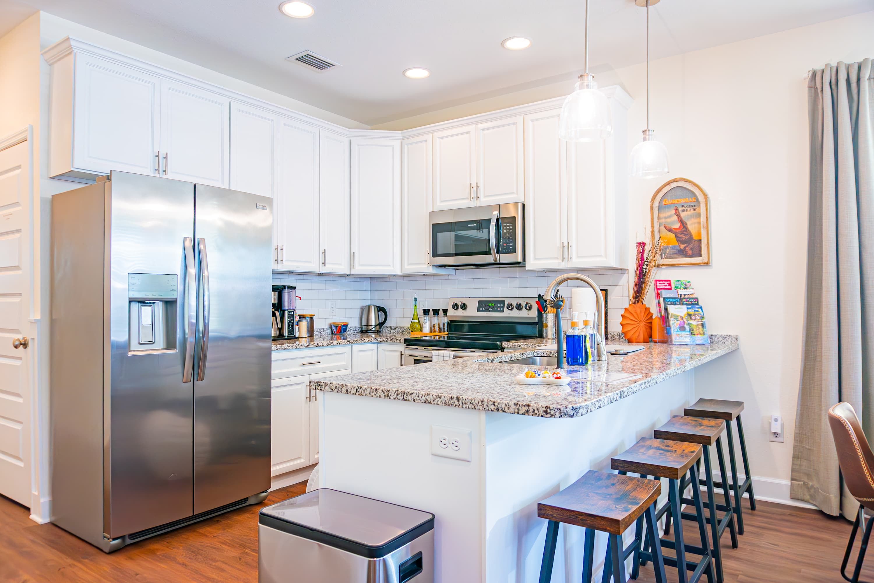 A modern kitchen with white cabinets, stainless steel appliances, a granite countertop, and bar stools.