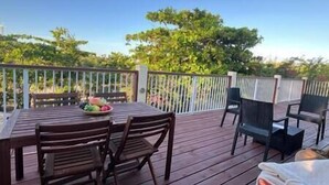 A wooden deck with a table and chairs, a fruit bowl, and a view of trees and sky. - 3bd/2ba Villa in the Bight - Alta 3 (The Bight Settlement)