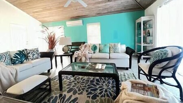 A living room with a white sofa, a glass coffee table, and a teal accent wall. - 3bd/2ba Villa in the Bight - Alta 3 (The Bight Settlement)