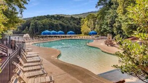 A swimming pool with lounge chairs and umbrellas, surrounded by trees and hills.