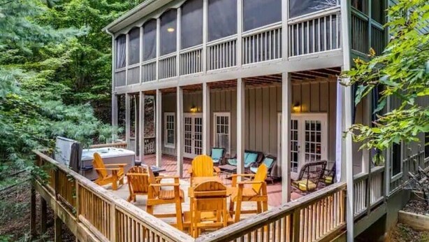 A covered outdoor deck with wooden chairs and a grill, surrounded by dense forest.