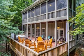 A covered outdoor deck with wooden chairs and a grill, surrounded by dense forest. - Big Canoe! 3 Masters, 2 Decks, Hot Tub, Fire Pit!
 (Big Canoe)