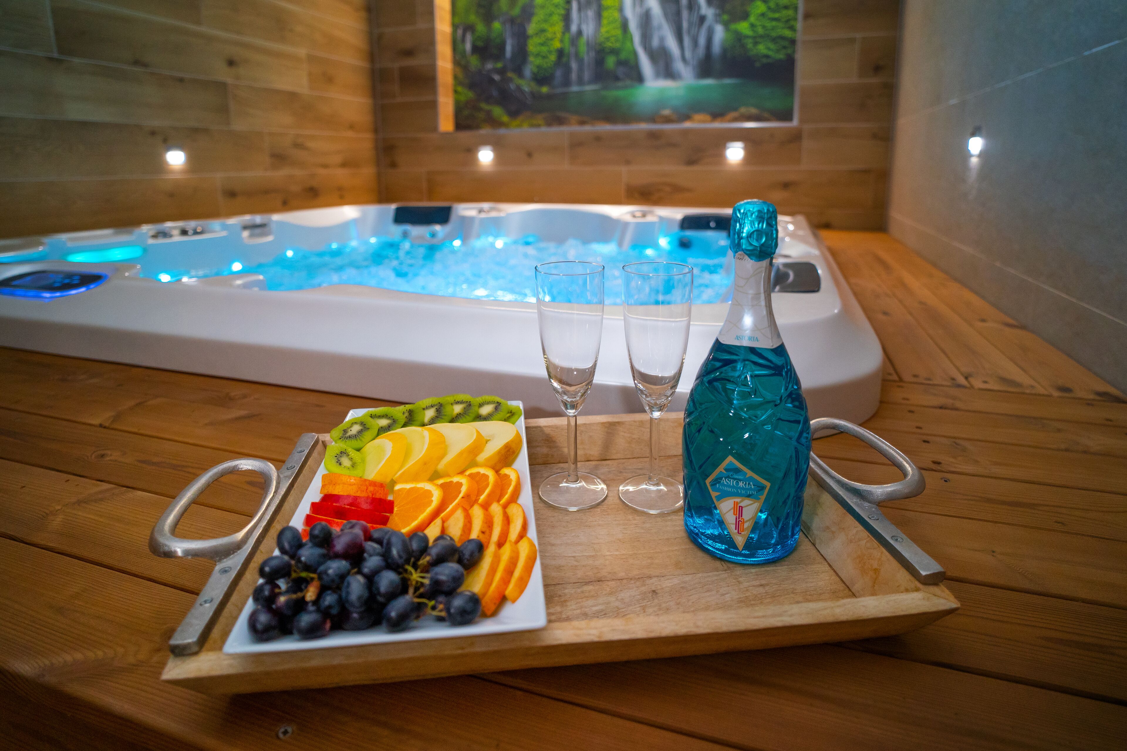 Ein Holztisch mit einer Obstplatte, zwei Gläsern und einer Flasche blauen Likörs vor einem Whirlpool mit blauer Beleuchtung.