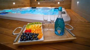 Ein Holztisch mit einer Obstplatte, zwei Gläsern und einer Flasche blauen Likörs vor einem Whirlpool mit blauer Beleuchtung.