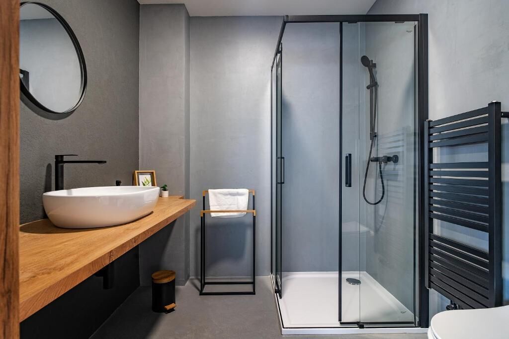 A modern bathroom with a large white sink, a glass shower enclosure, and a wooden vanity.