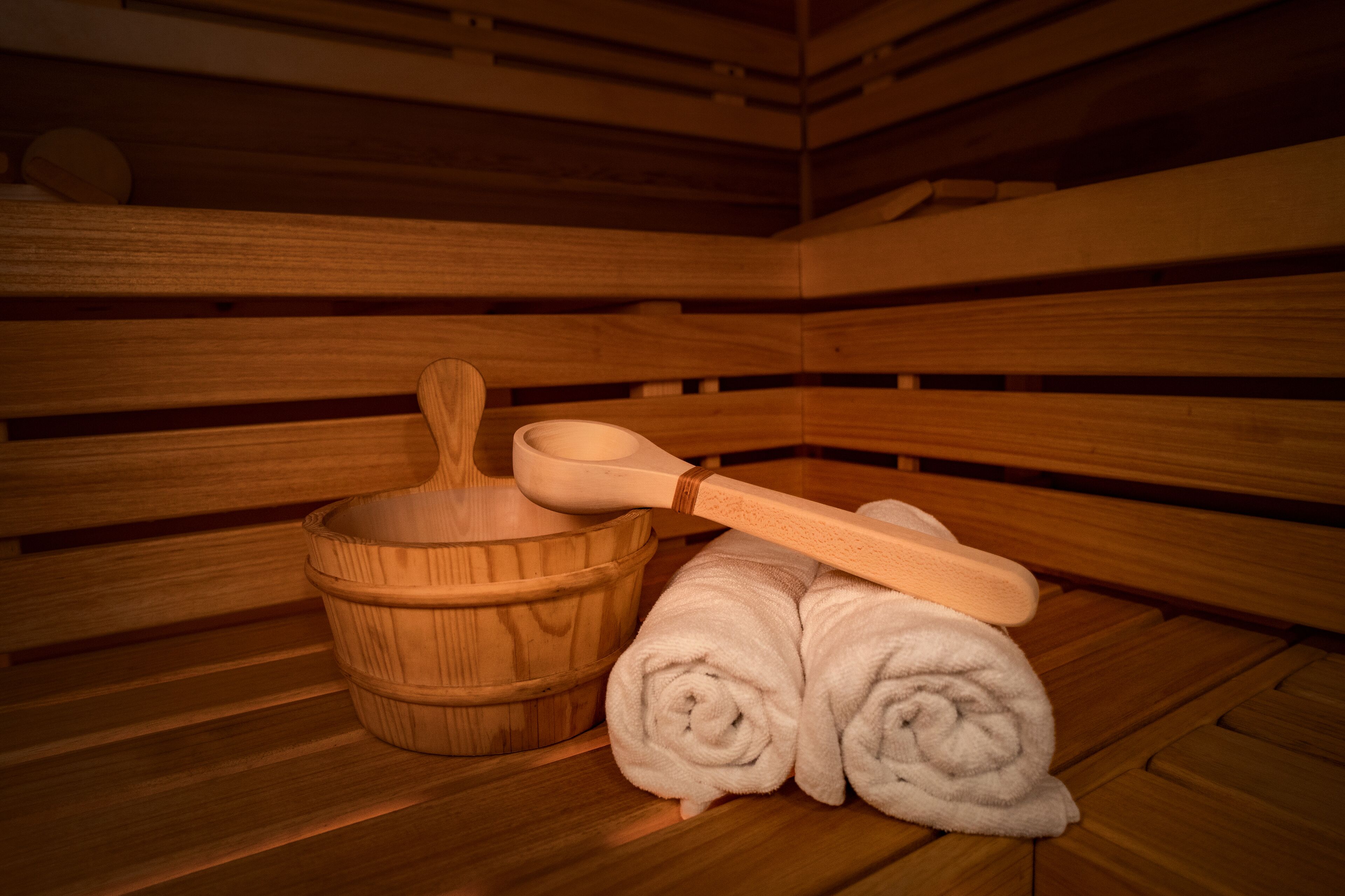 A wooden sauna with a wooden bench, a wooden basin, and rolled towels.