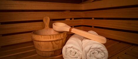 A wooden sauna with a wooden bench, a wooden basin, and rolled towels.