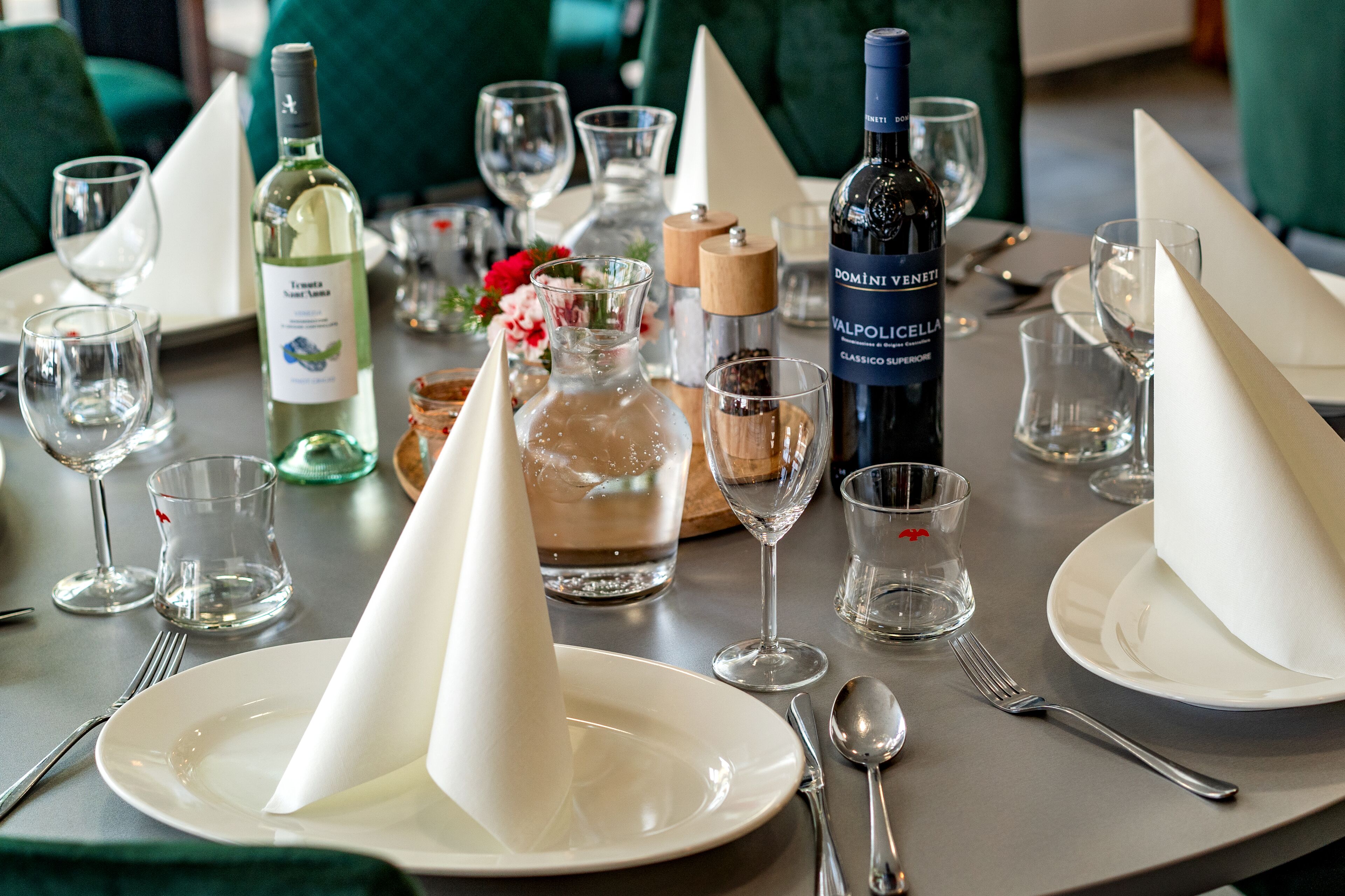 Una mesa dispuesta para comer, con botellas de vino, copas y un centro de mesa con flores.