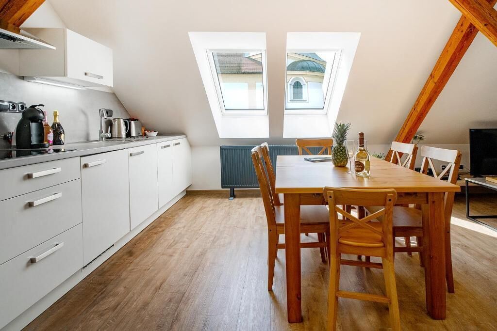 Une cuisine moderne avec des meubles blancs, une table à manger en bois et quatre chaises, ainsi que deux puits de lumière.
