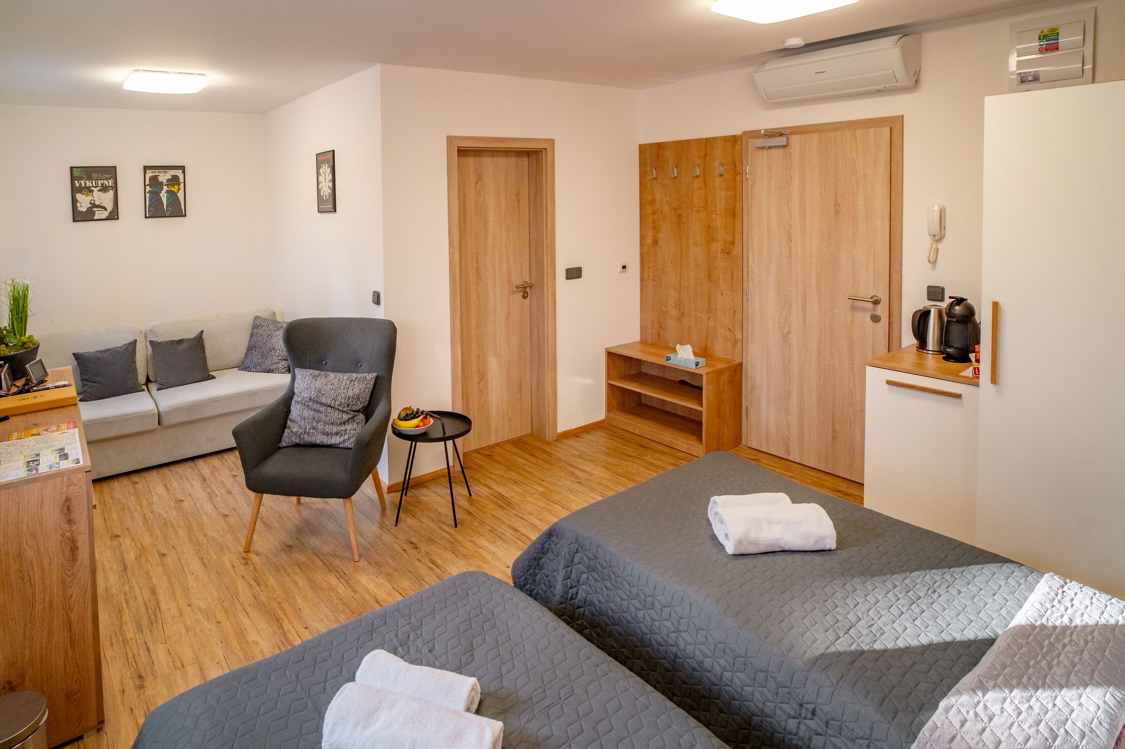 Ett hotellrum med två sängar, en soffa, en fåtölj, ett litet bord, en garderob och ett litet kök.