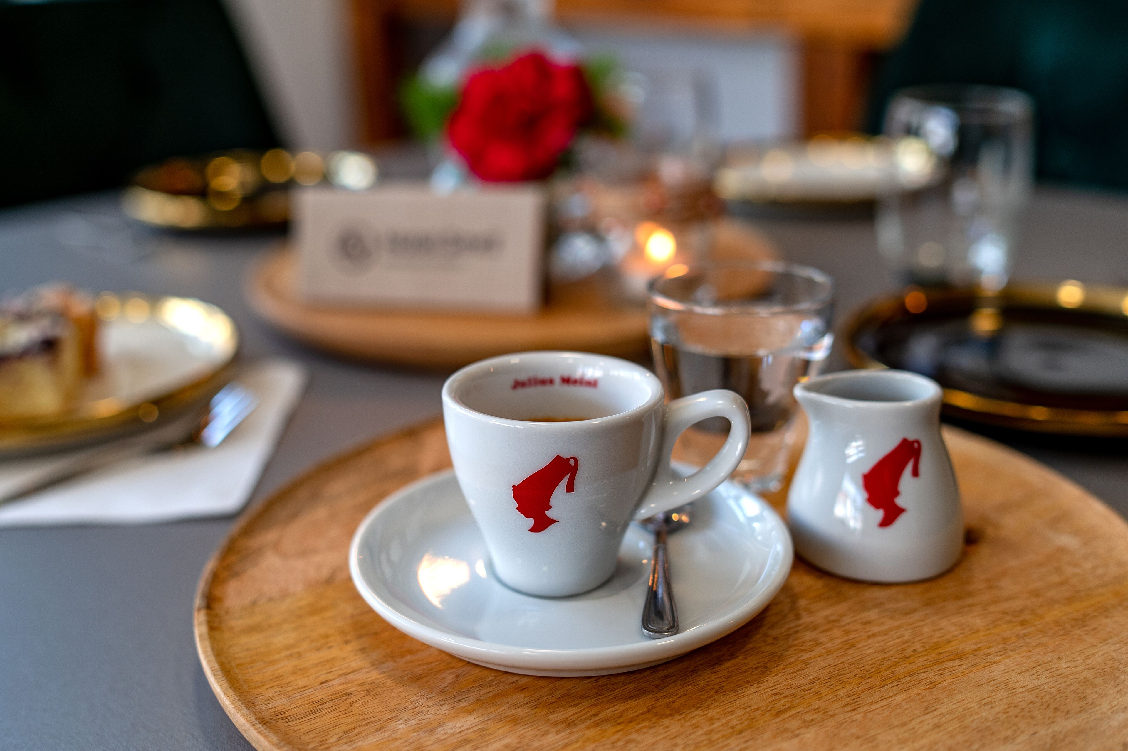 A table setting with two white cups featuring a red logo, a small white cup, and a glass of water on a wooden tray.