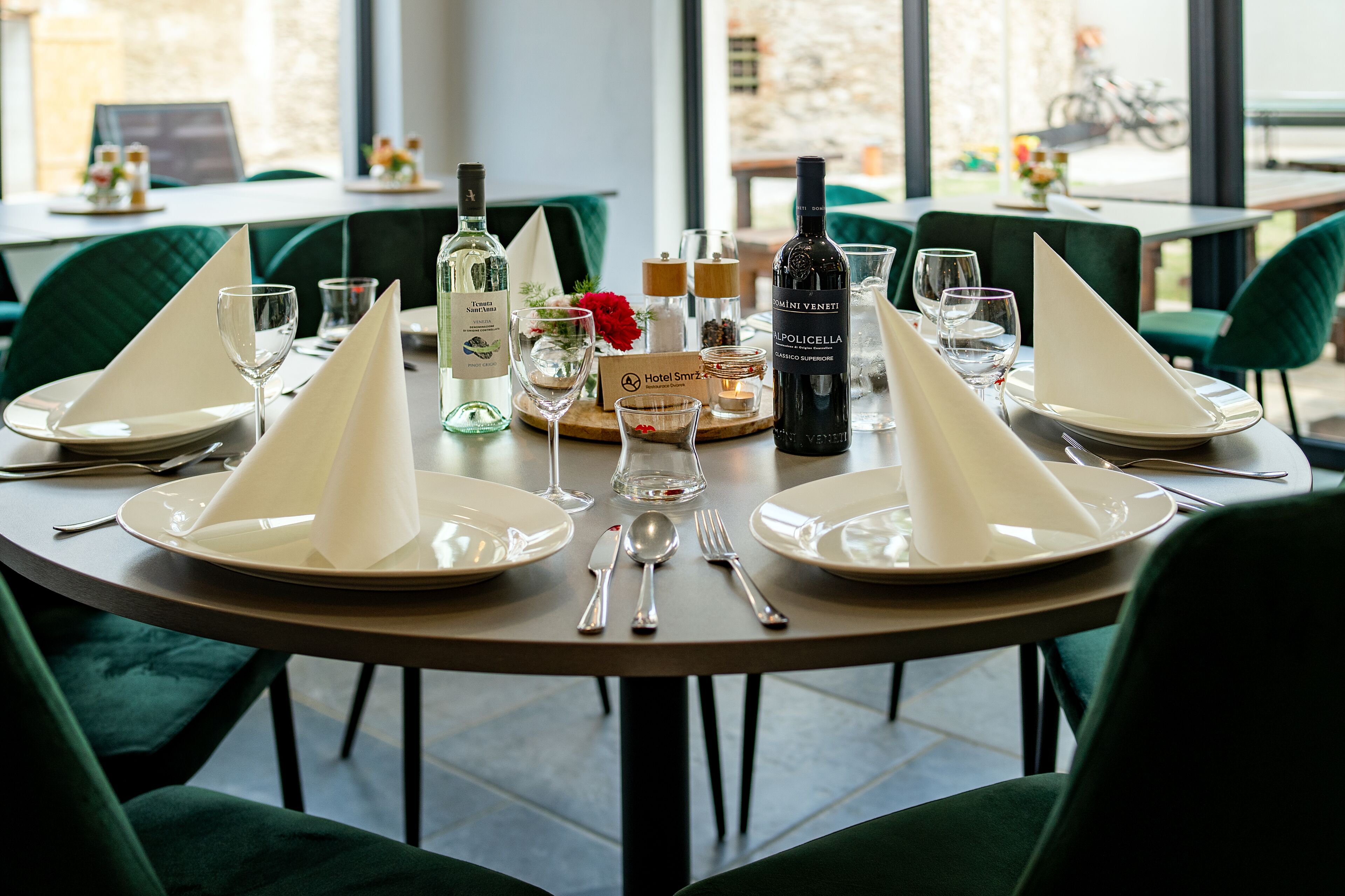 A dining table set with white napkins, plates, cutlery, and wine glasses, with a bottle of wine and a candle on the table.