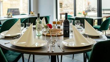 A dining table set with white napkins, plates, cutlery, and wine glasses, with a bottle of wine and a candle on the table.