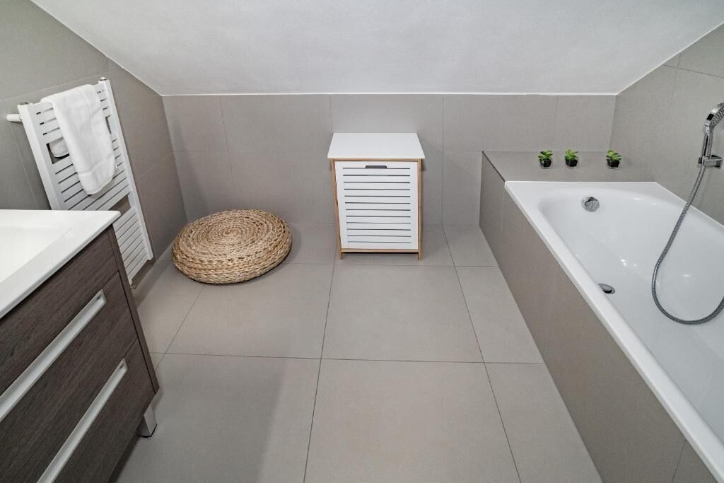 A modern bathroom with a bathtub, a small wooden cabinet, a woven basket, and a towel rack.