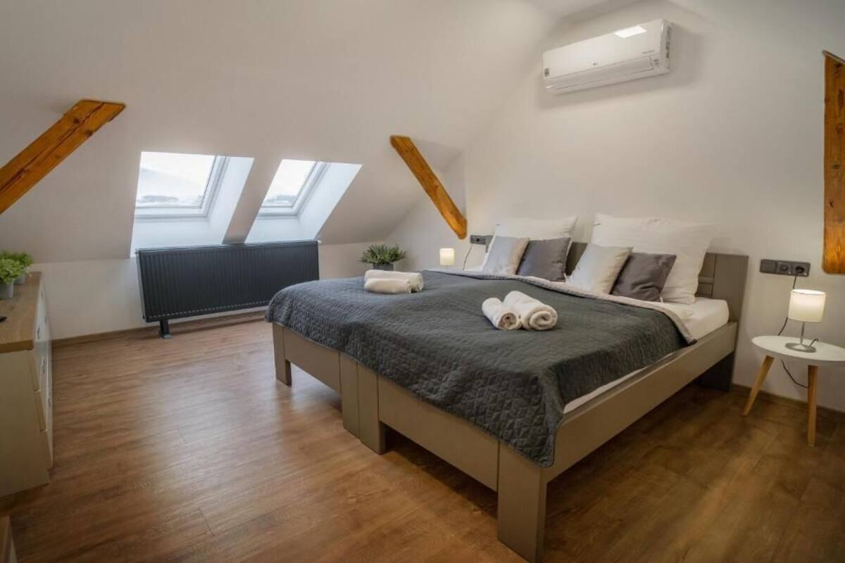 Quarto com cama, claraboia, radiador e uma pequena mesa de cabeceira com abajur.