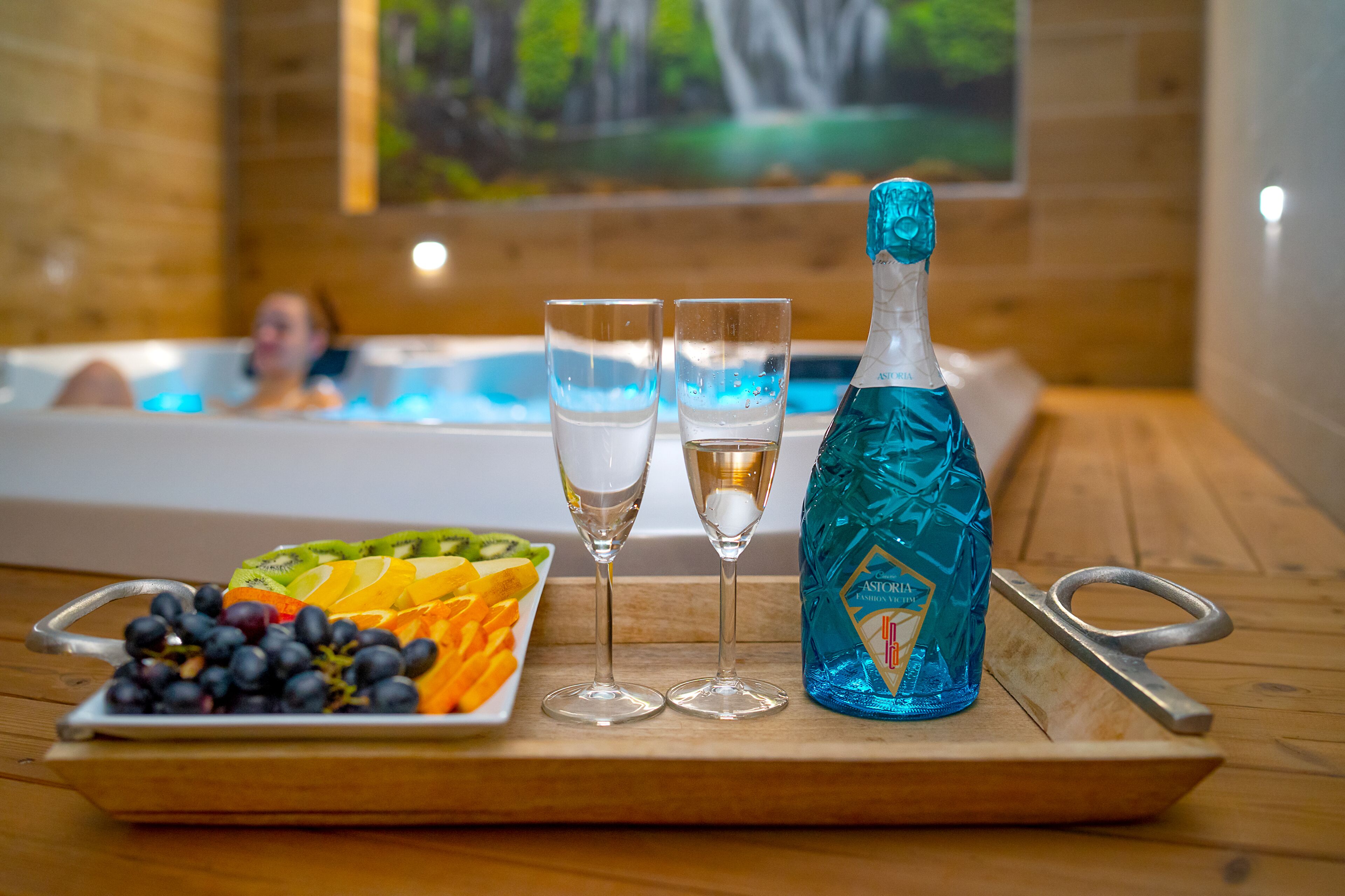 A tray with a bottle of champagne, two glasses, and a fruit platter on a wooden table.