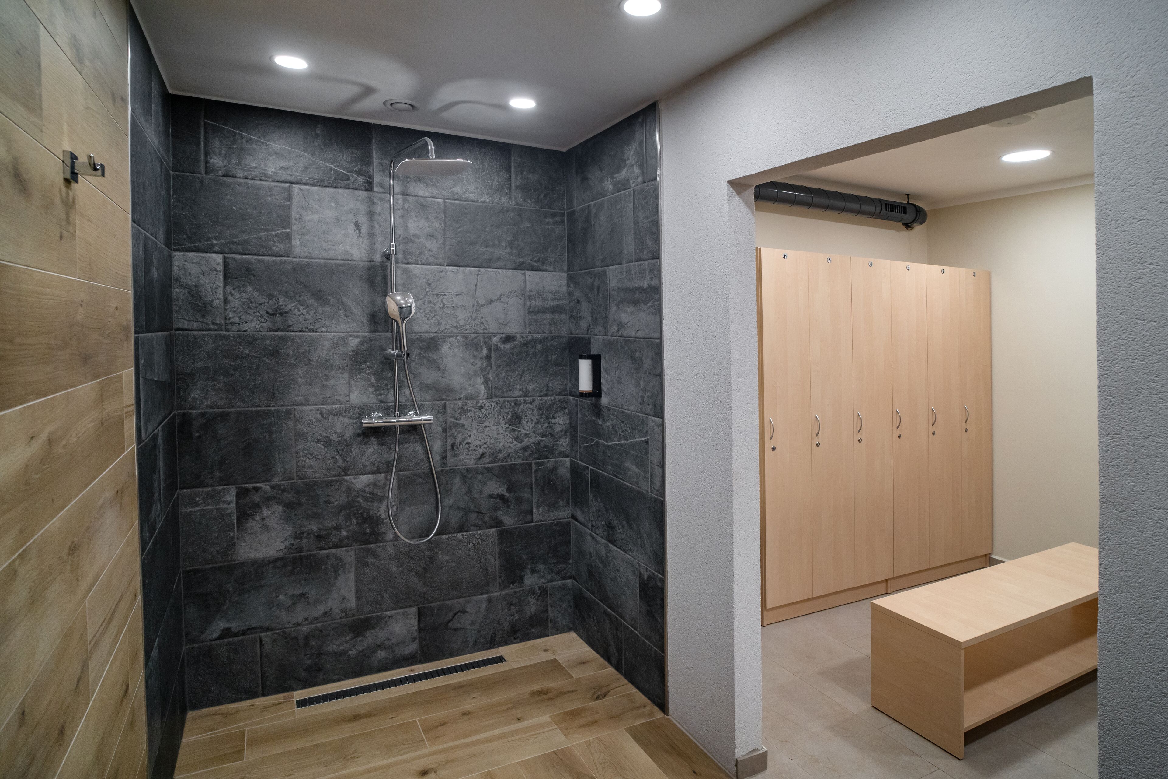 A modern bathroom with a shower, wooden cabinets, and a bench.