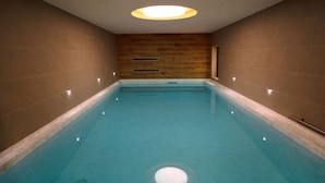 A rectangular indoor swimming pool with a wooden wall and a ceiling light fixture.