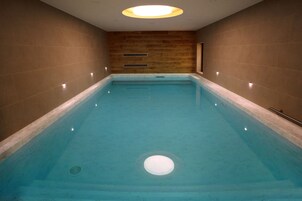 A rectangular indoor swimming pool with a wooden wall and a ceiling light fixture.