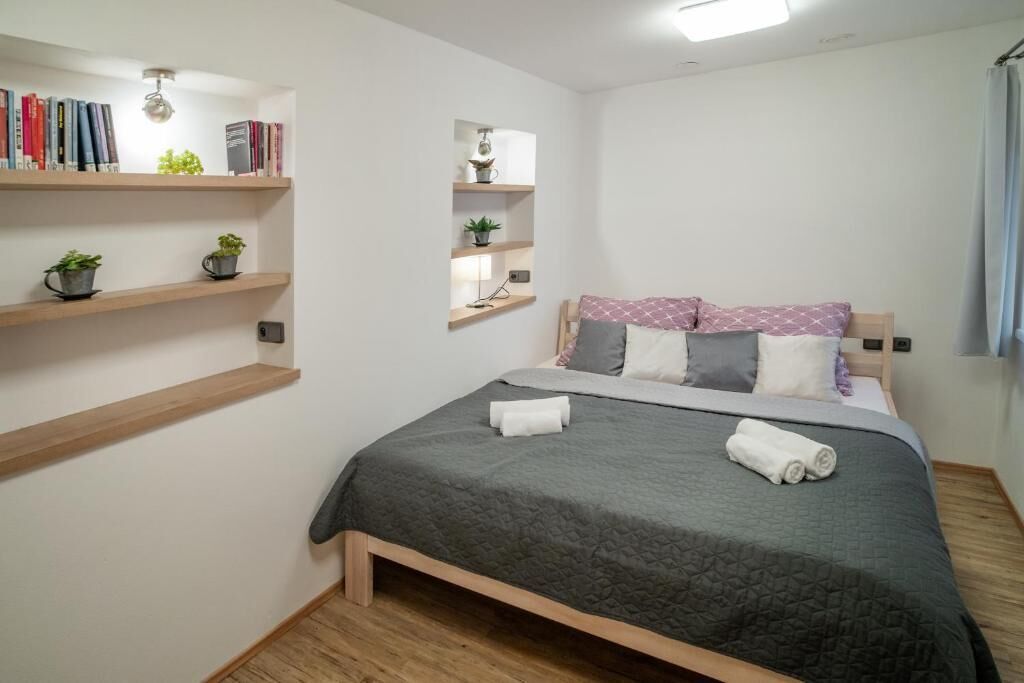 A bedroom with a bed, shelves with books and plants, and a bedside lamp.