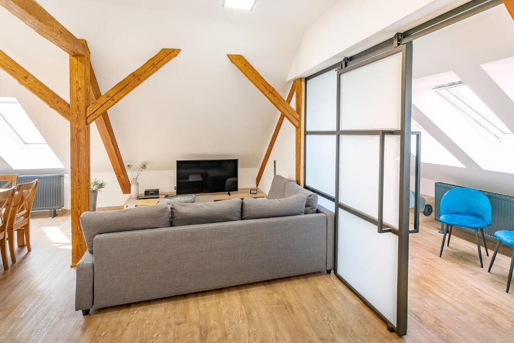 Una sala de estar moderna con un sofá gris, un televisor de pantalla plana, vigas de madera y un amplio ventanal corredero.
