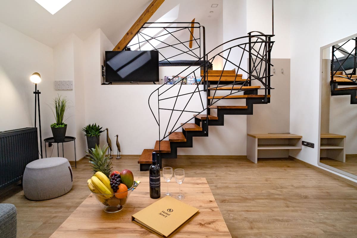 Uma sala de estar moderna com uma escada em espiral, uma TV de tela plana na parede, uma mesa de jantar de madeira com uma fruteira e uma pequena planta em vaso.