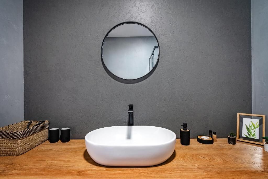 A modern bathroom with a round mirror, a white sink, and a wooden countertop.