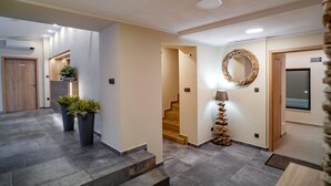 A modern hotel lobby with a staircase, potted plants, a mirror, and a wooden door.