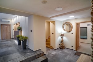 A modern hotel lobby with a staircase, potted plants, a mirror, and a wooden door.