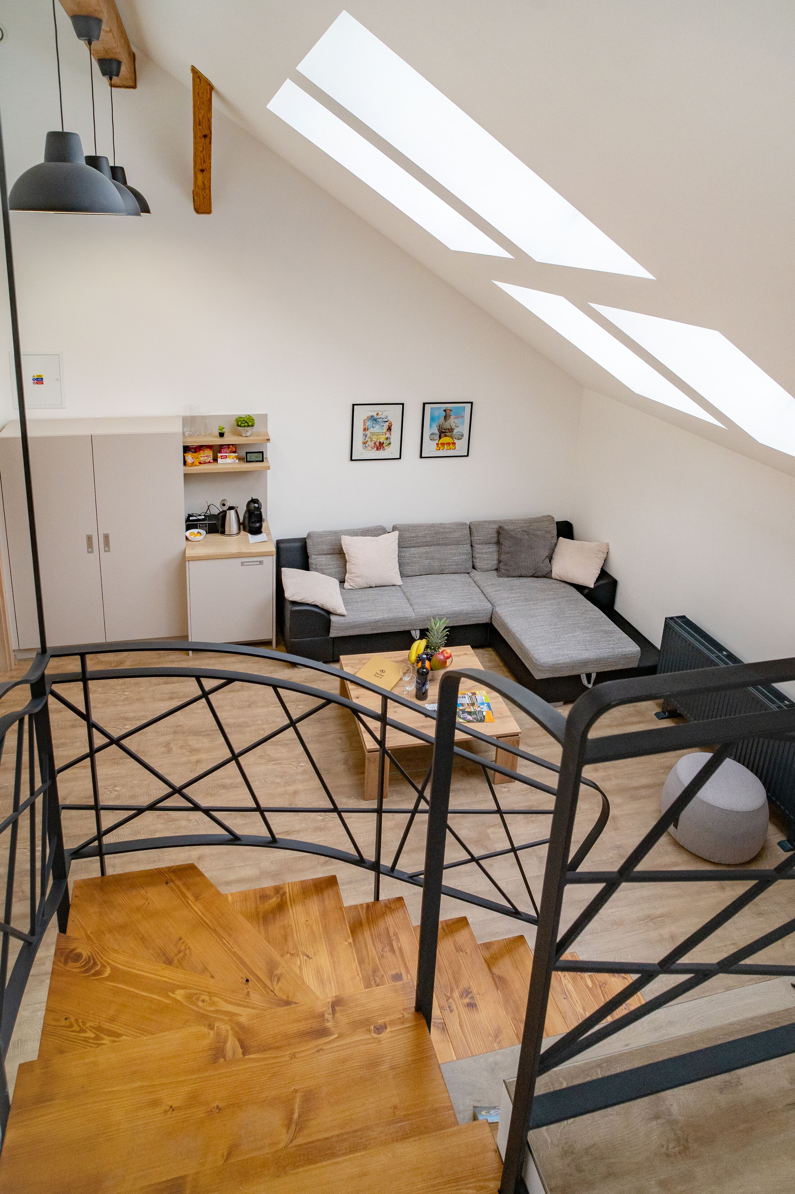 Un moderno apartamento tipo loft con escalera, un sofá seccional gris, una mesa de centro de madera y una zona de cocina.